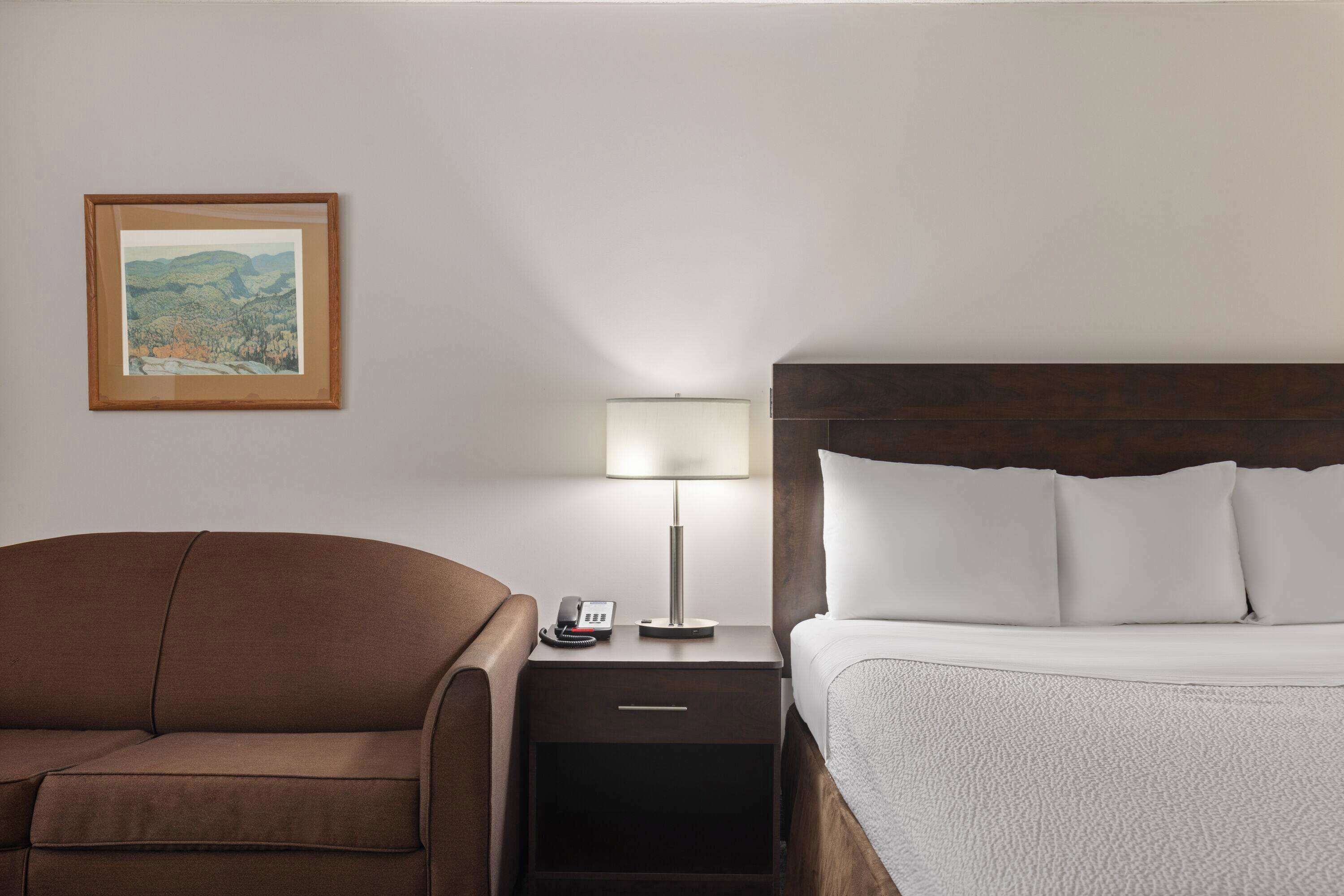 A hotel room with a bed, a nightstand with a lamp, a phone, and a framed picture on the wall.