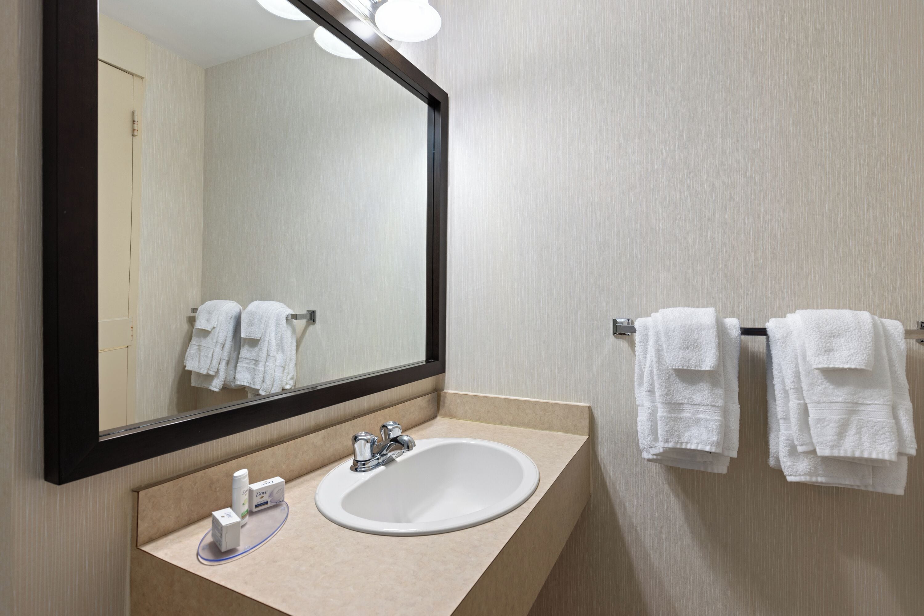 A bathroom with a large mirror, a sink, and two towels hanging on a towel rack.