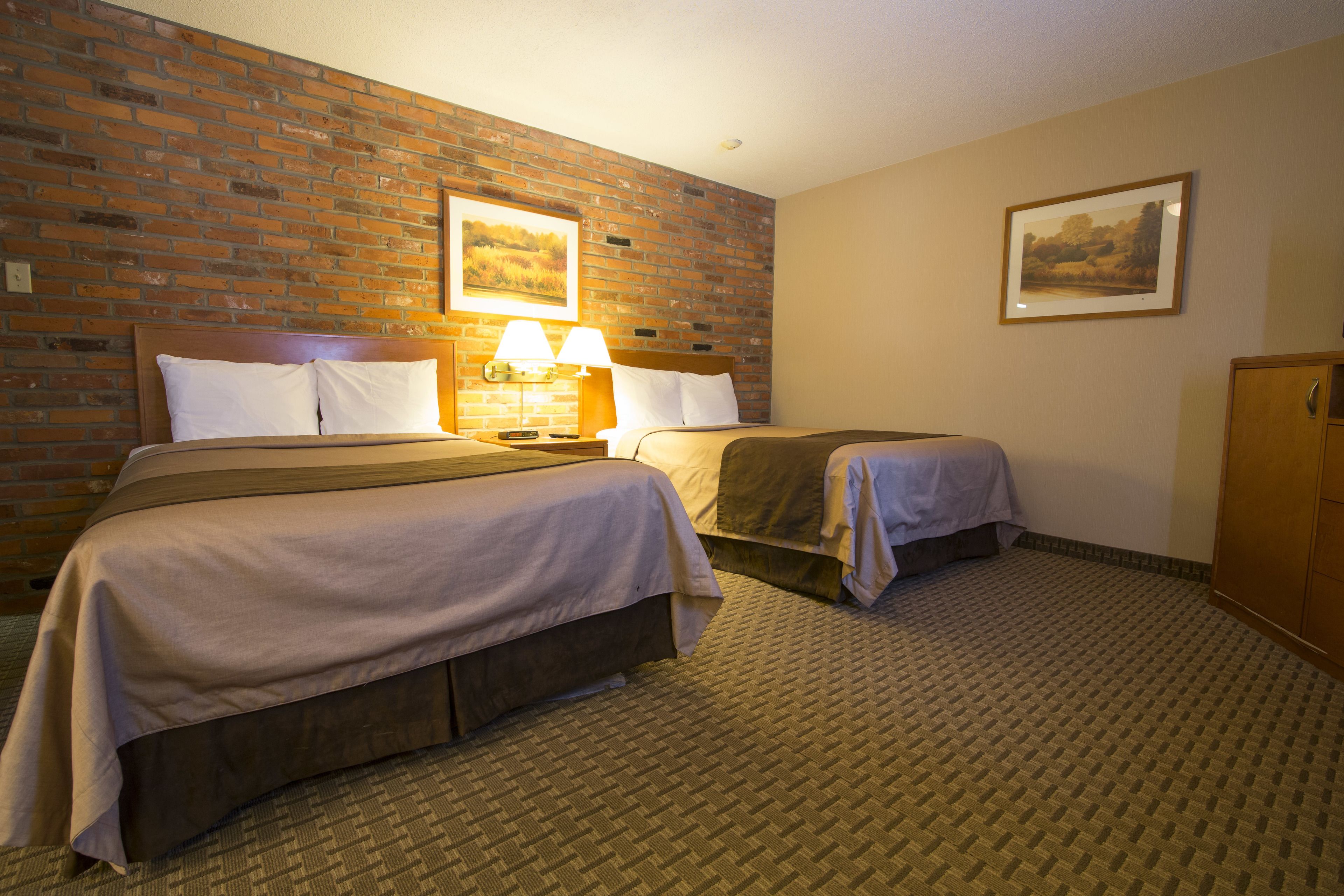 Une chambre d’hôtel avec deux lits, un mur en briques, un tableau encadré et une lampe.