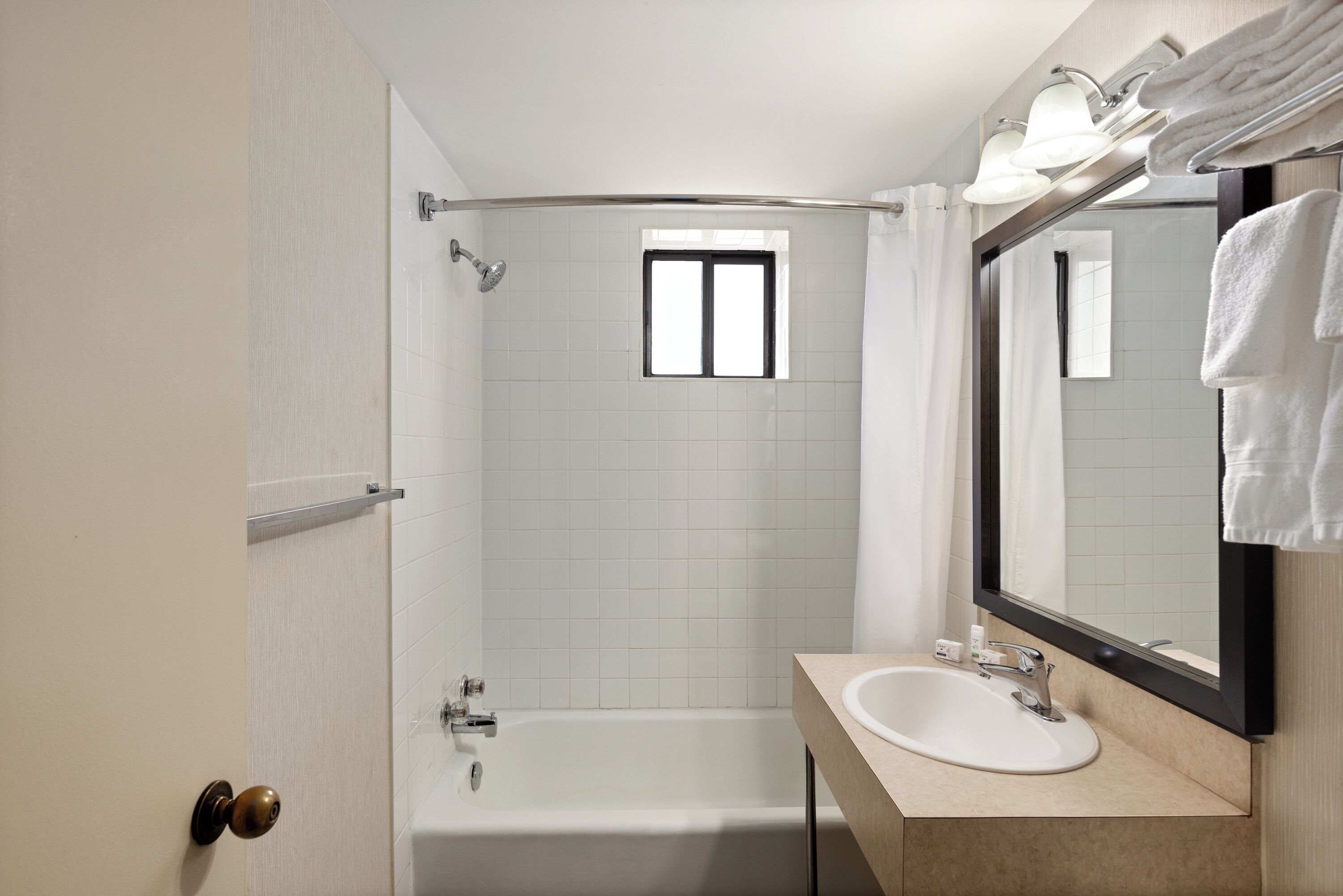 A bathroom with a bathtub, a sink, a mirror, and a window.