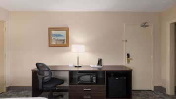 Quarto de hotel com cama, escrivaninha com cadeira, micro-ondas, cafeteira e porta.