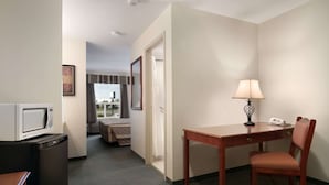 Habitación de hotel con kitchenette, un escritorio con lámpara, una silla y una cama con vistas al exterior.