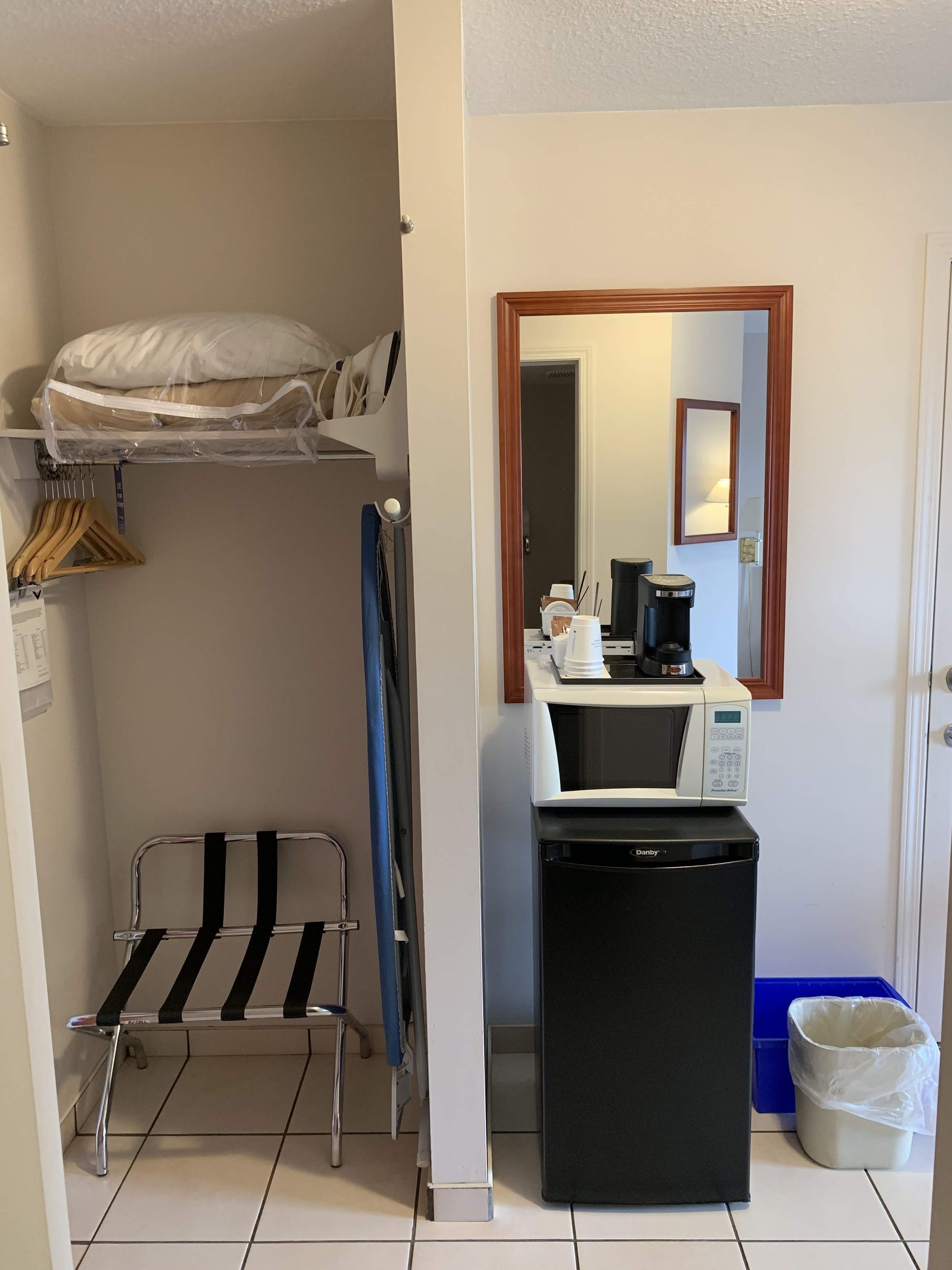 A compact hotel room with a bunk bed, a small kitchenette, a mirror, and a trash bin.