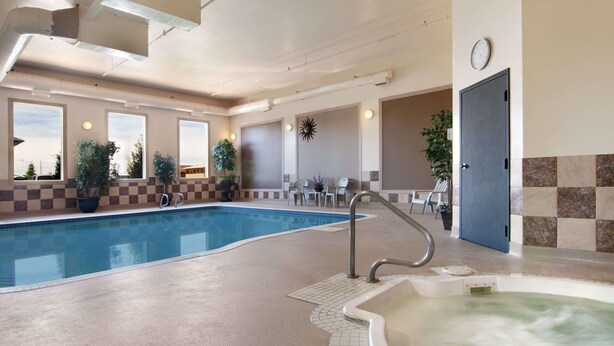 Una piscina interior con hidromasaje, azulejos de diseño cuadriculado, plantas en macetas y un reloj en la pared.
