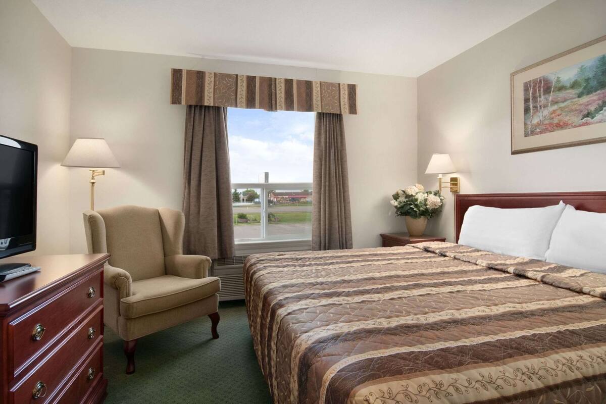 Habitación de hotel con cama, una silla, televisor, escritorio y ventana con cortinas.