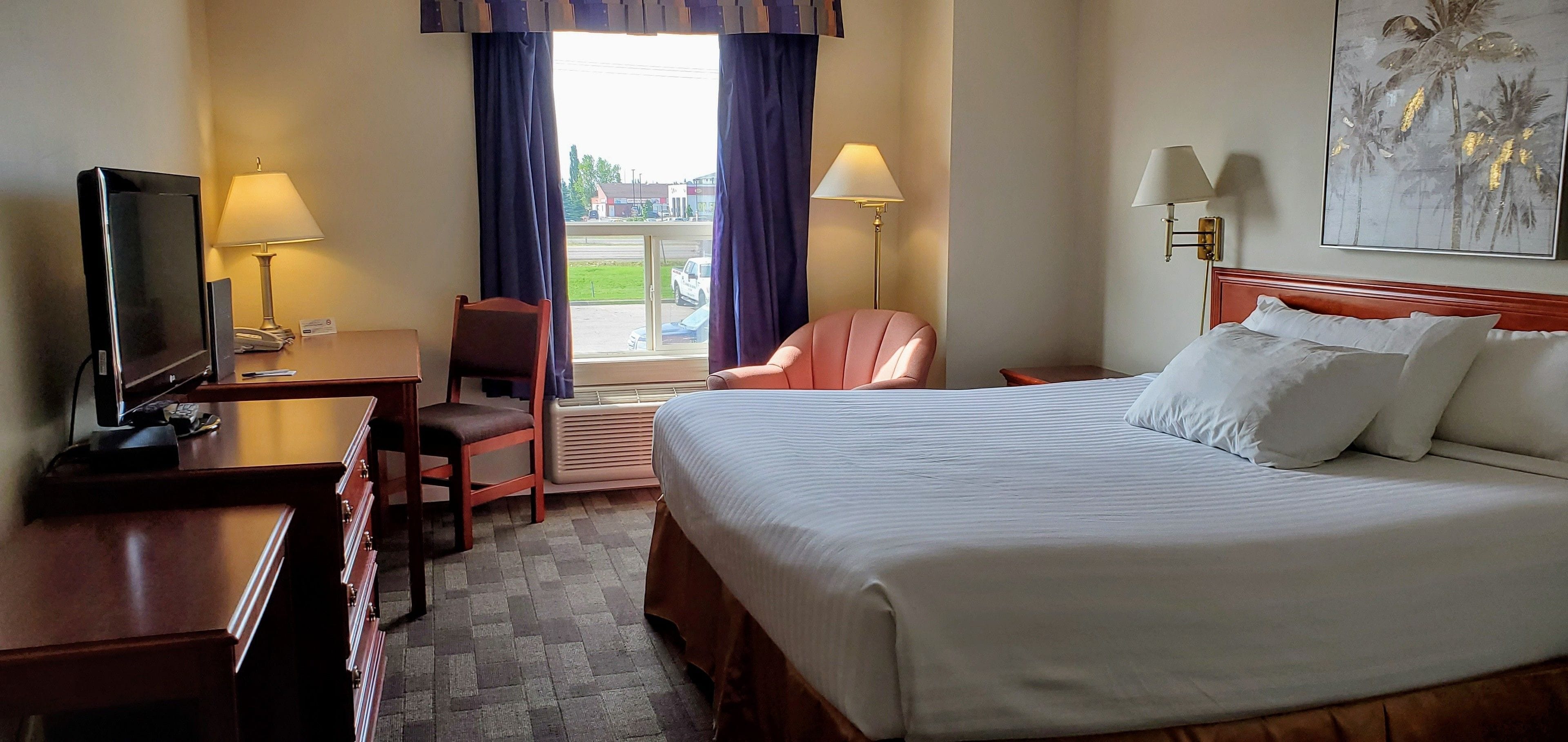 A hotel room with a bed, desk, chair, TV, and two lamps.
