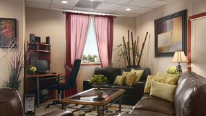Un salón con un sofá de cuero marrón, una mesa de centro, un televisor sobre un soporte de madera, una estantería y una ventana con cortinas rosadas.