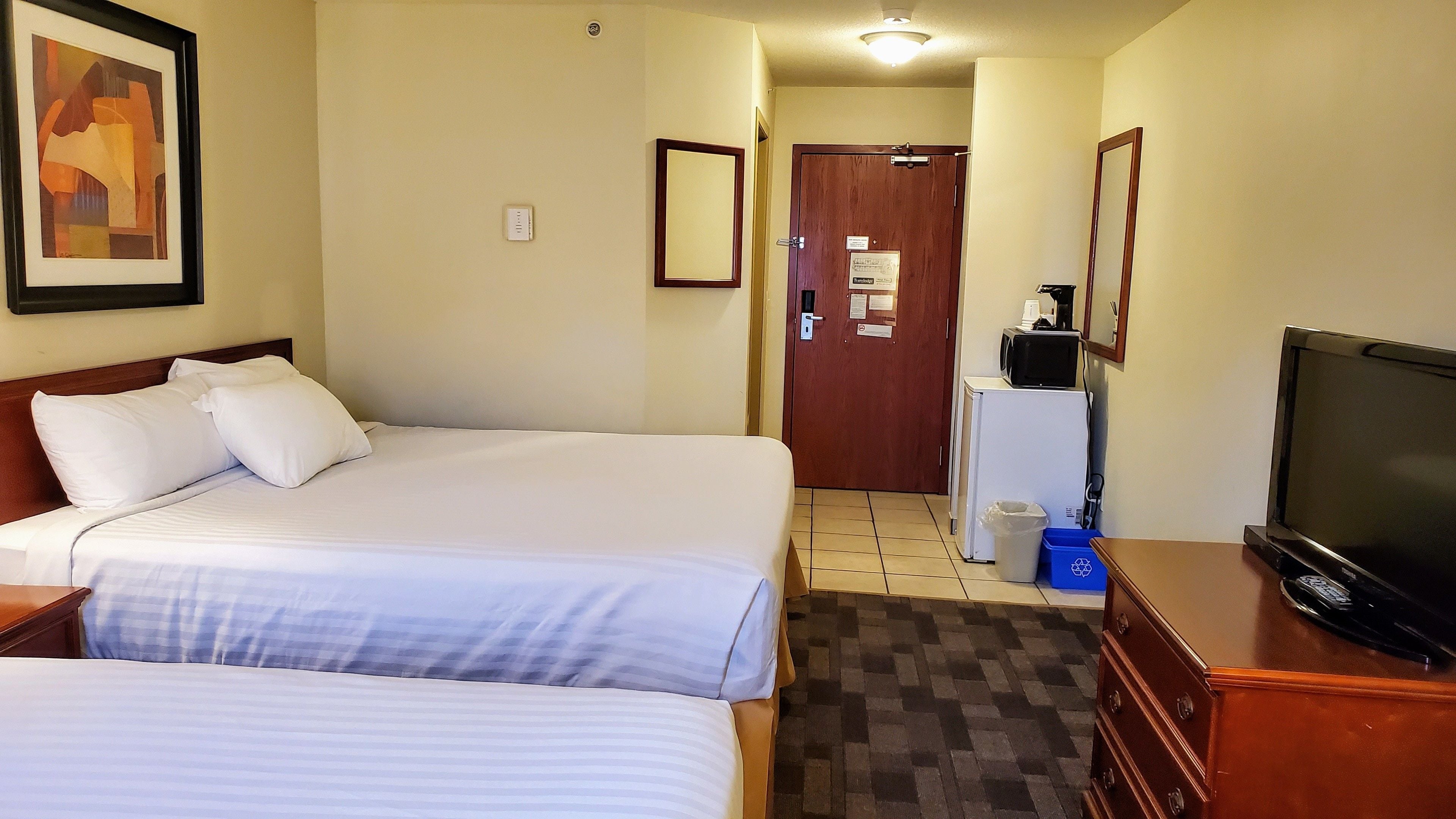 A hotel room with two beds, a television, a refrigerator, and a microwave.