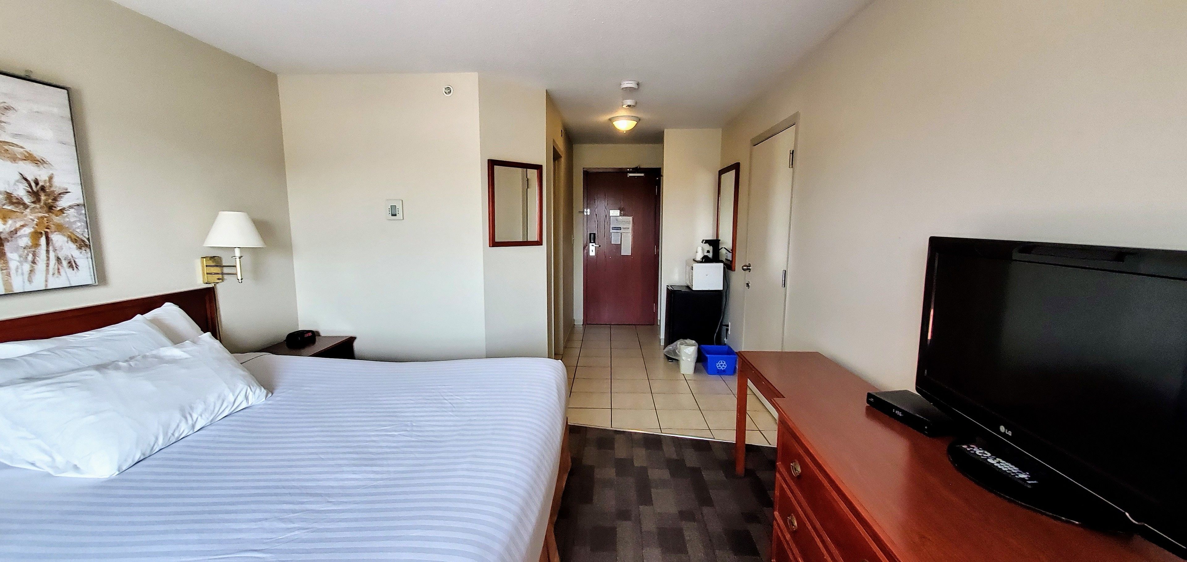 A hotel room with a bed, a TV, a desk, and a bathroom visible in the background.