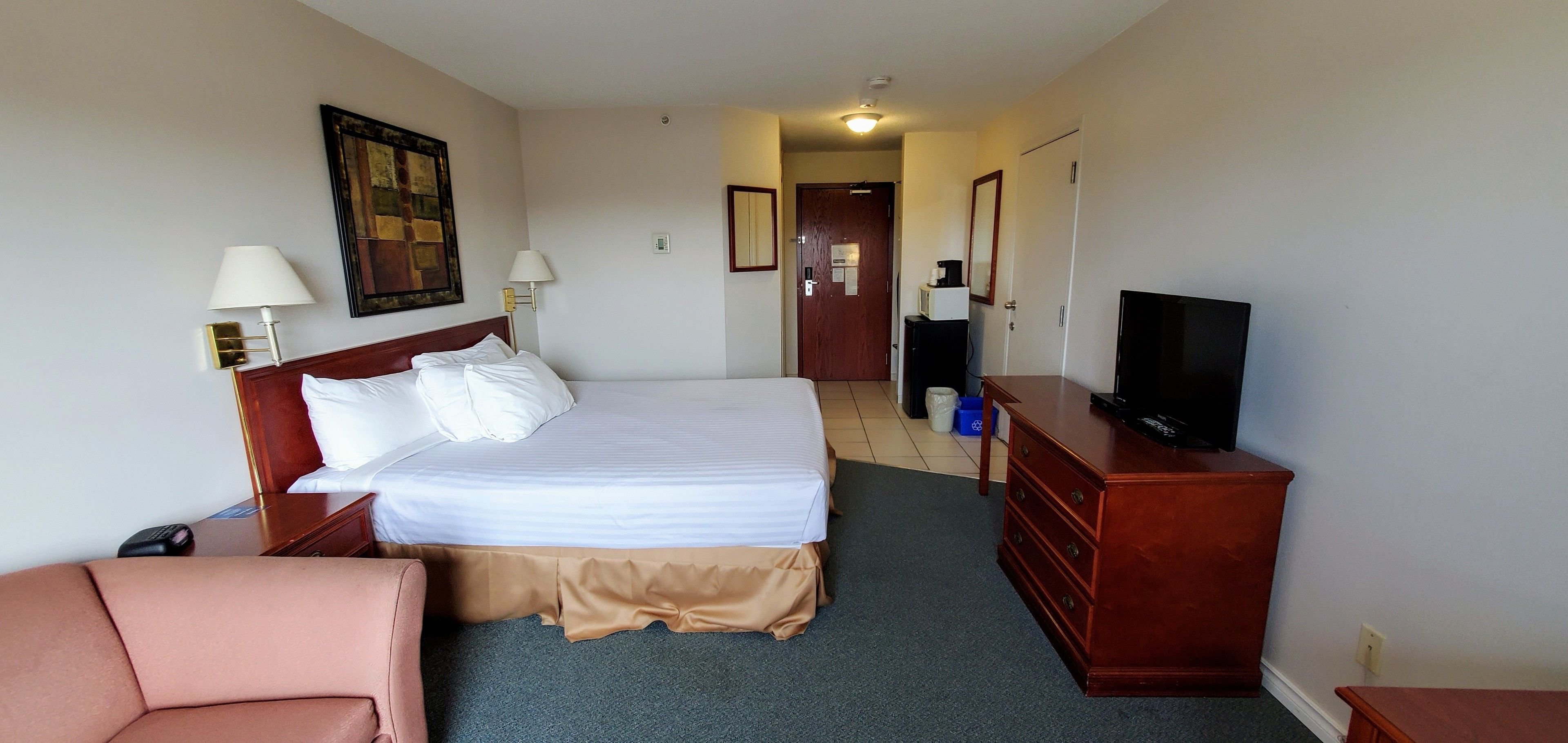 Ein Hotelzimmer mit einem Bett, Nachttischlampen, einem Fernseher, einem Schminktisch und einer Tür zu einem anderen Raum.