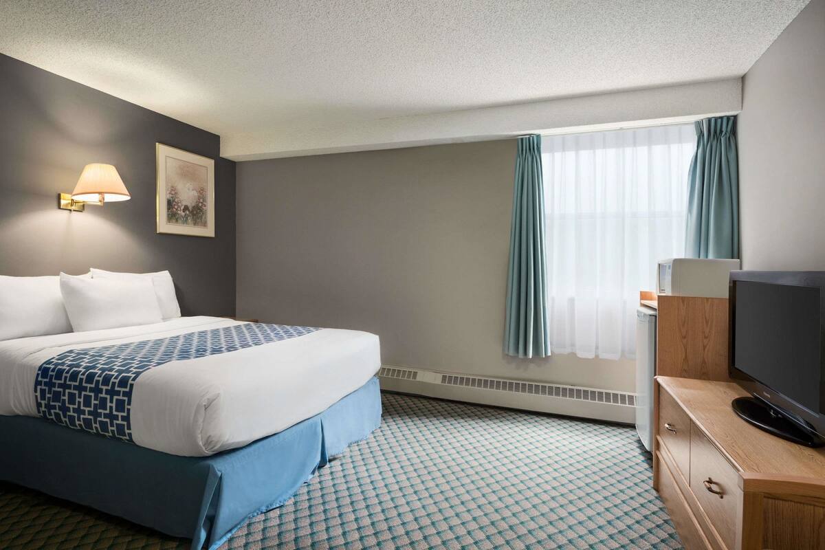 A hotel room with a bed, a television, a heater, and a window with curtains.