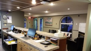 A reception desk with computers, a clock, and a window with a view of the outside.