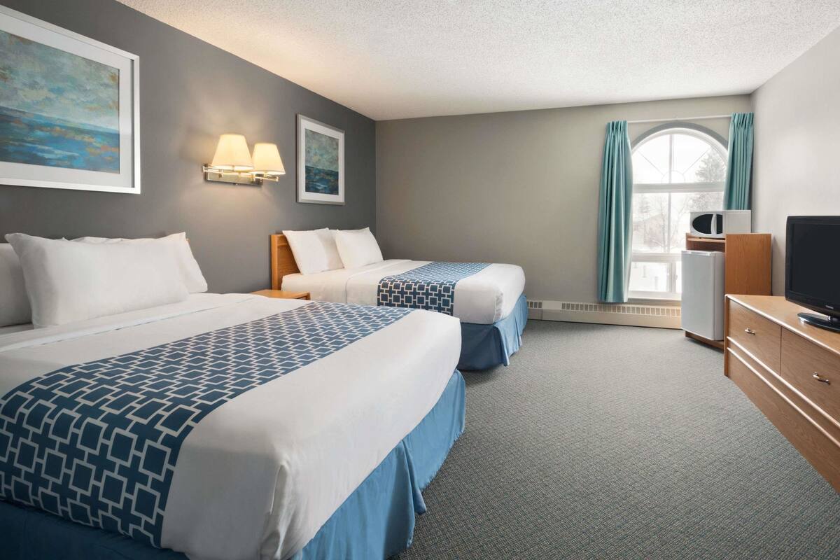 A hotel room with two beds, a television, a desk, and a window with curtains.