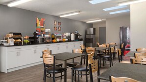 A modern kitchen with white cabinets, a central island, and a seating area with wooden chairs and tables.