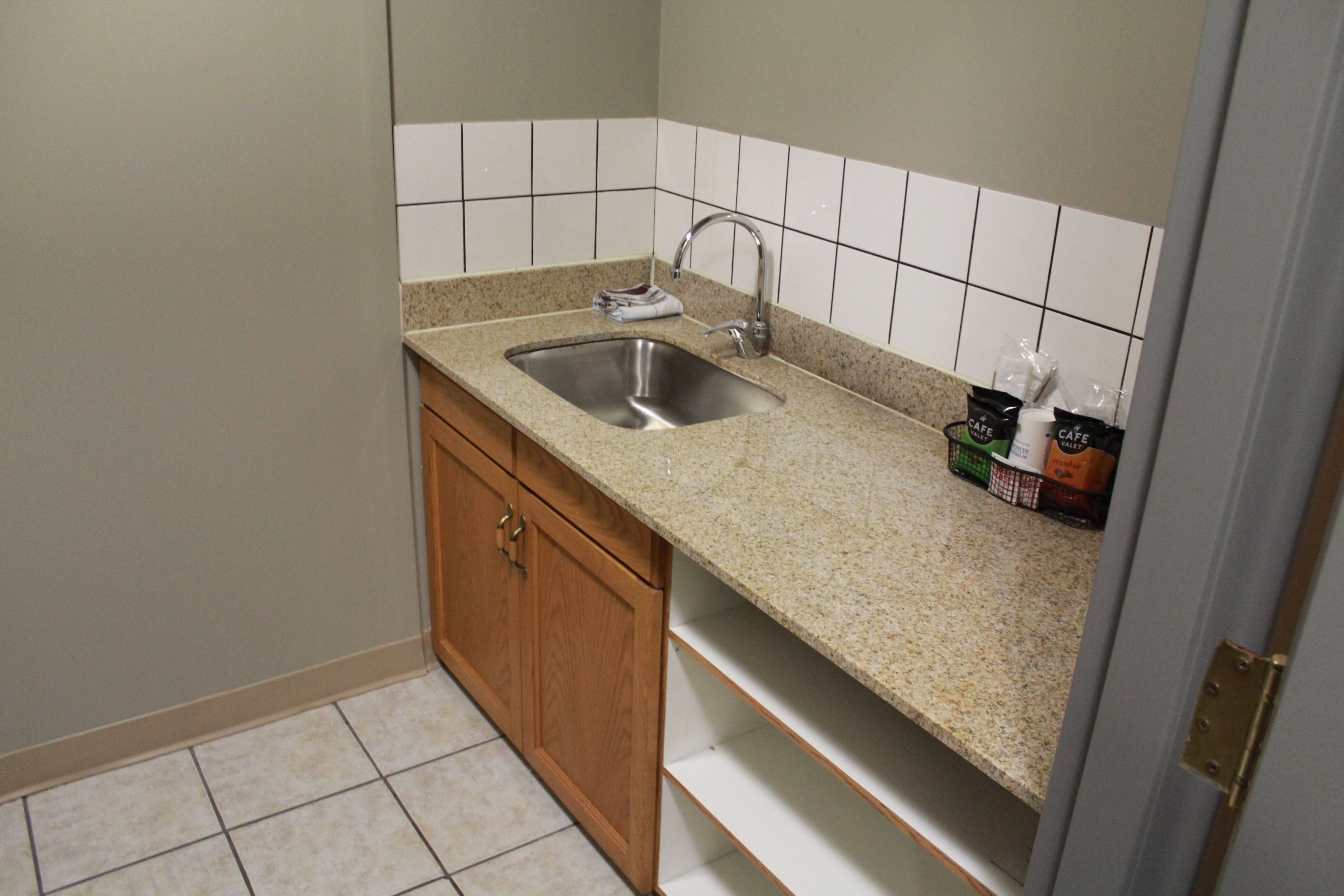Una cocina con encimera de granito, pileta de acero inoxidable, muebles de madera y salpicadero azulejado.