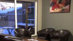 A room with a wooden table and leather chairs, a window with a view of a snowy landscape, and a painting on the wall.