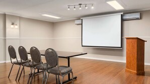 A conference room with a wooden table, four chairs, a podium, a projector screen, and ceiling lights. - Travelodge by Wyndham Owen Sound (Owen Sound)