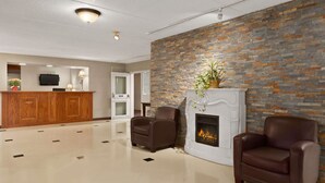 A lobby with a reception desk, two leather armchairs, a fireplace, and a stone wall. - Travelodge by Wyndham Owen Sound (Owen Sound)