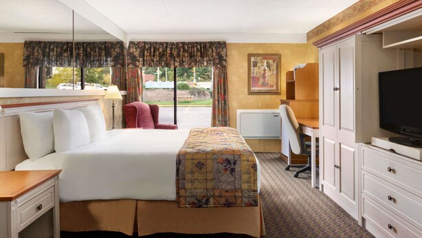 A hotel room with a large bed, a desk with a chair, a television, and a wardrobe. - Travelodge by Wyndham Owen Sound (Owen Sound)