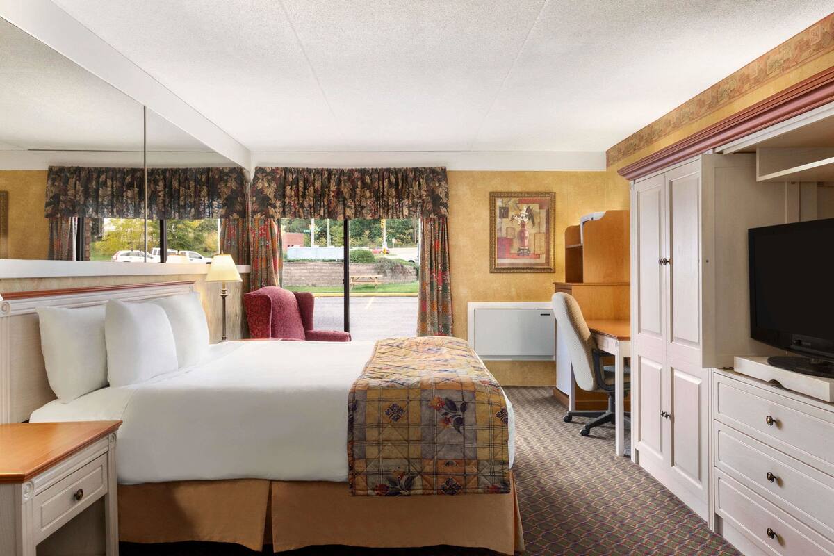 Une chambre d’hôtel avec un grand lit, un bureau avec une chaise, une télévision et une armoire.