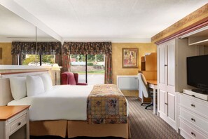 A hotel room with a large bed, a desk with a chair, a television, and a wardrobe.