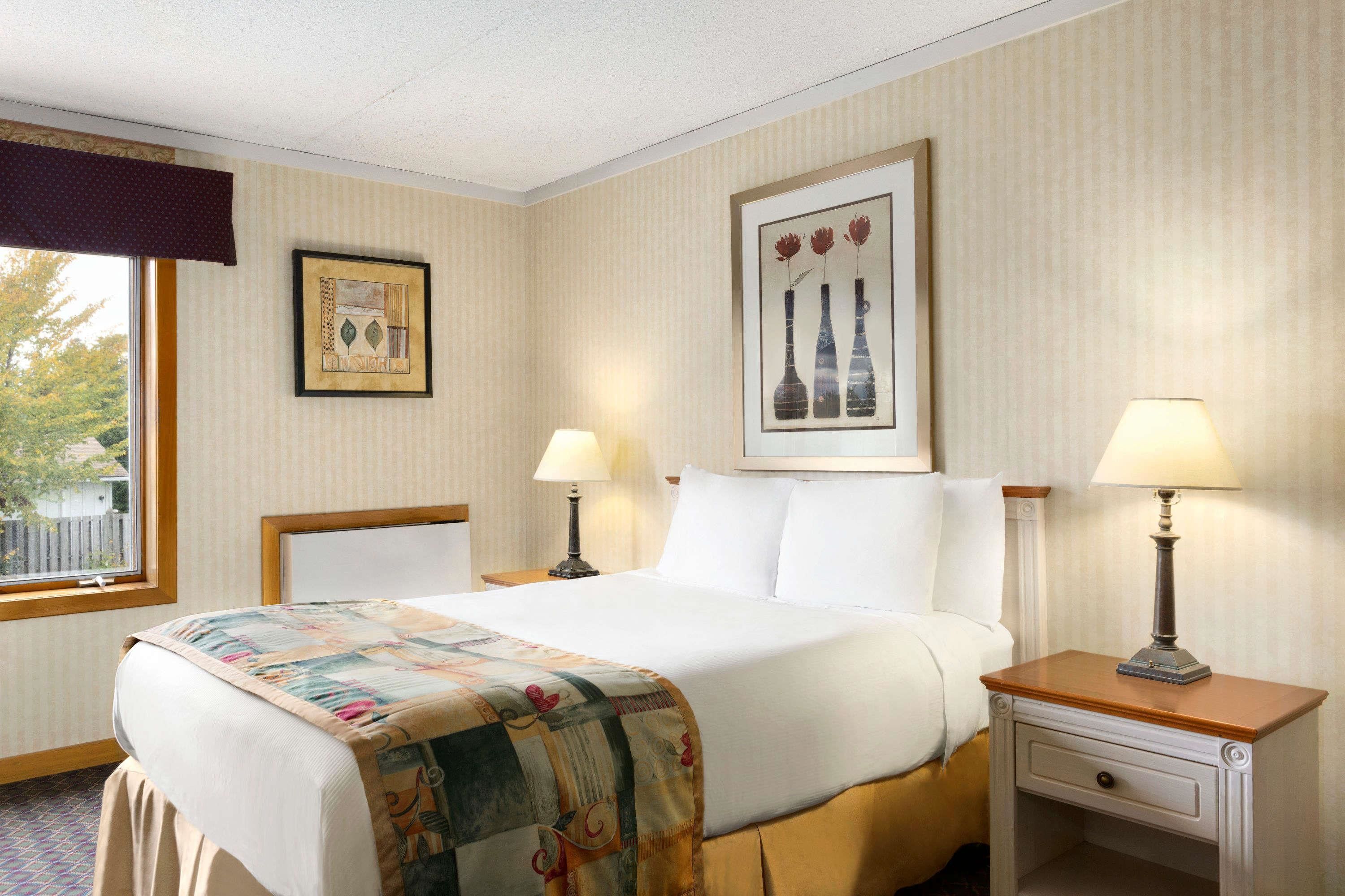 A hotel room with a large bed, two bedside tables with lamps, a window with a view of trees, and a framed picture on the wall.