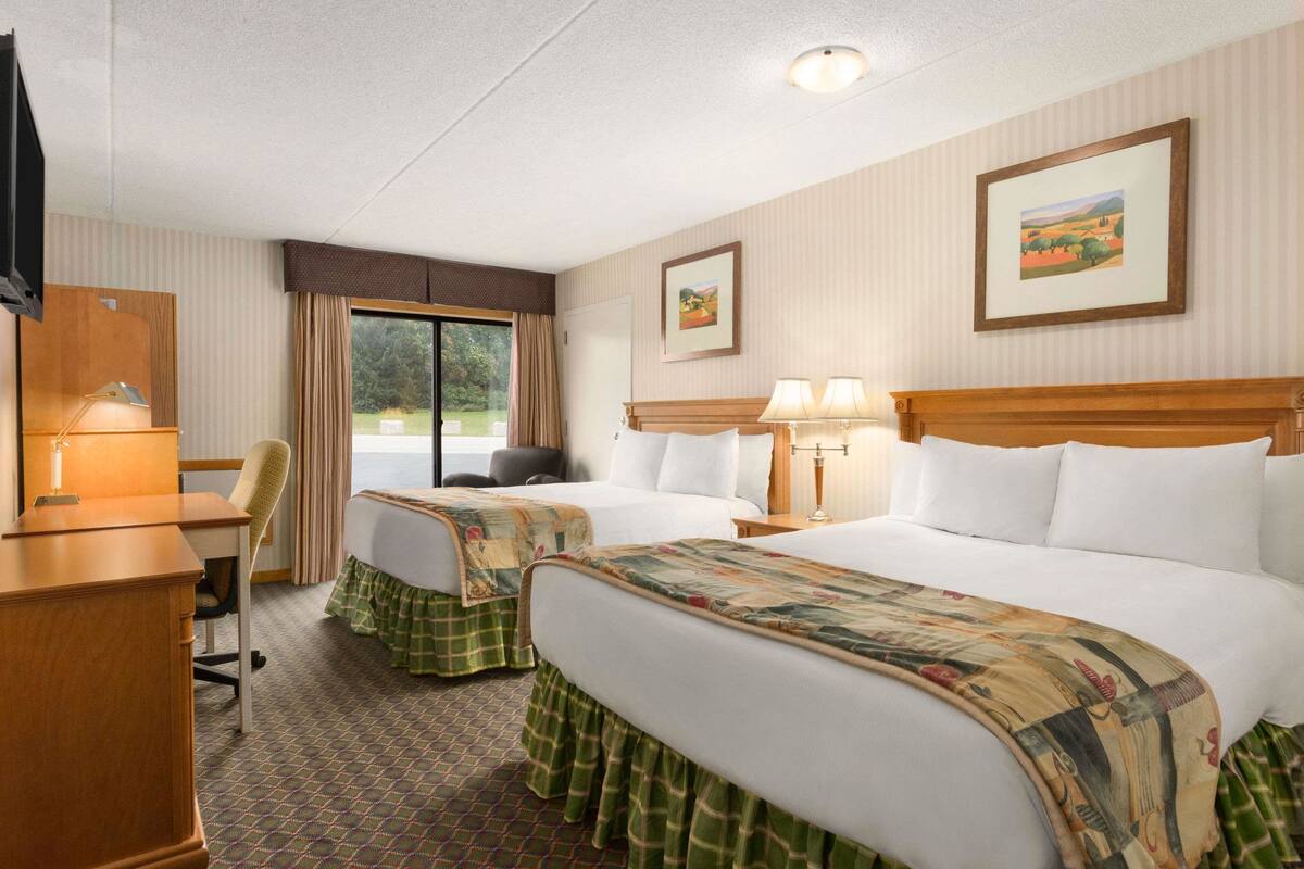 Une chambre d’hôtel avec deux lits, un bureau, une chaise, une télévision et une fenêtre avec des rideaux.