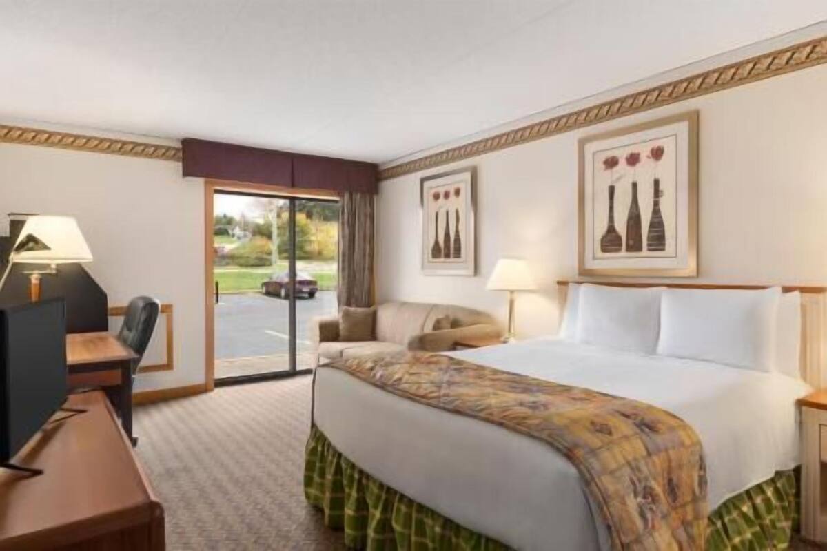 Une chambre d’hôtel avec un lit, un bureau avec une chaise, une lampe et une vue à travers une porte vitrée.