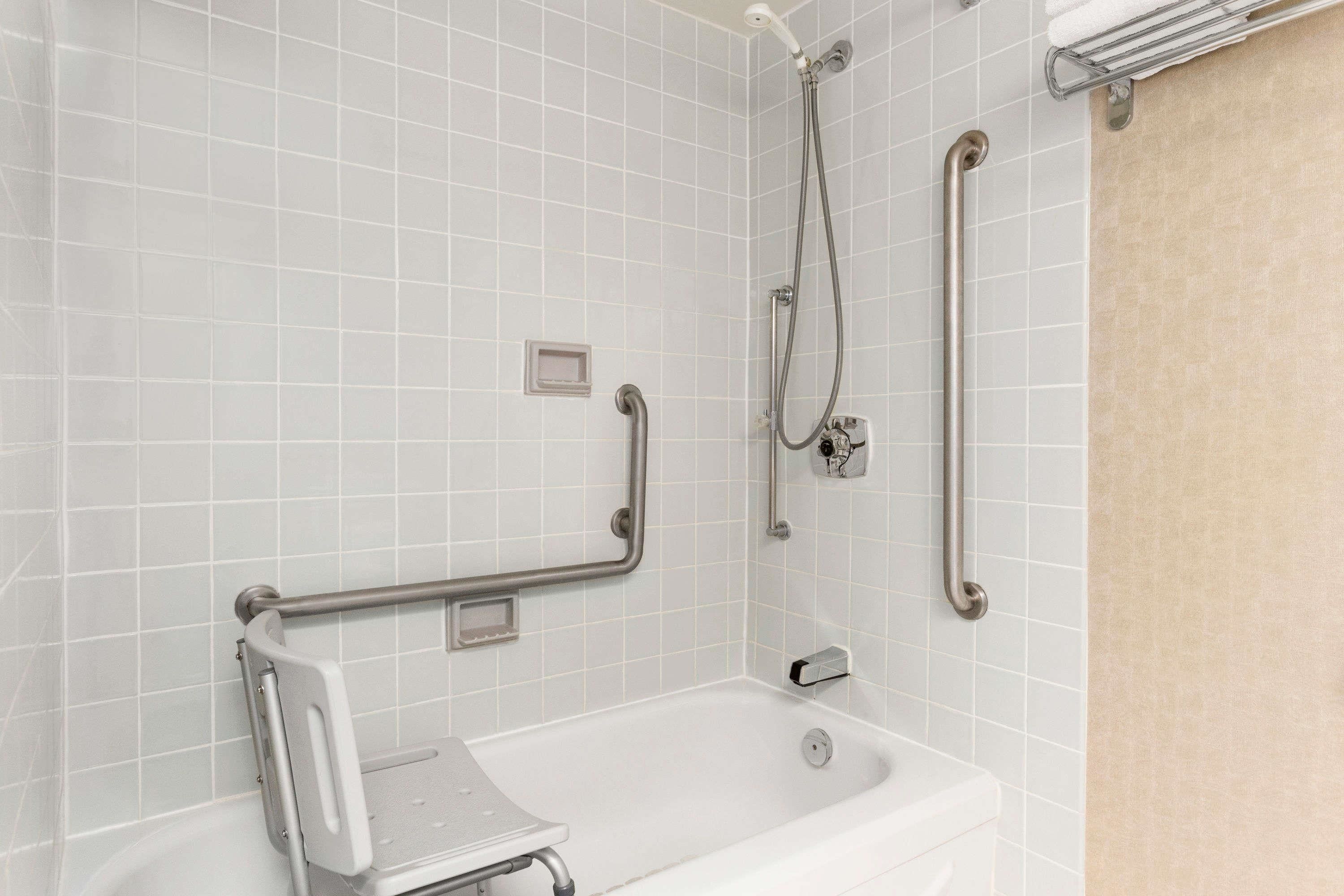 A bathroom with white tiled walls, a white bathtub, and a shower with grab bars.