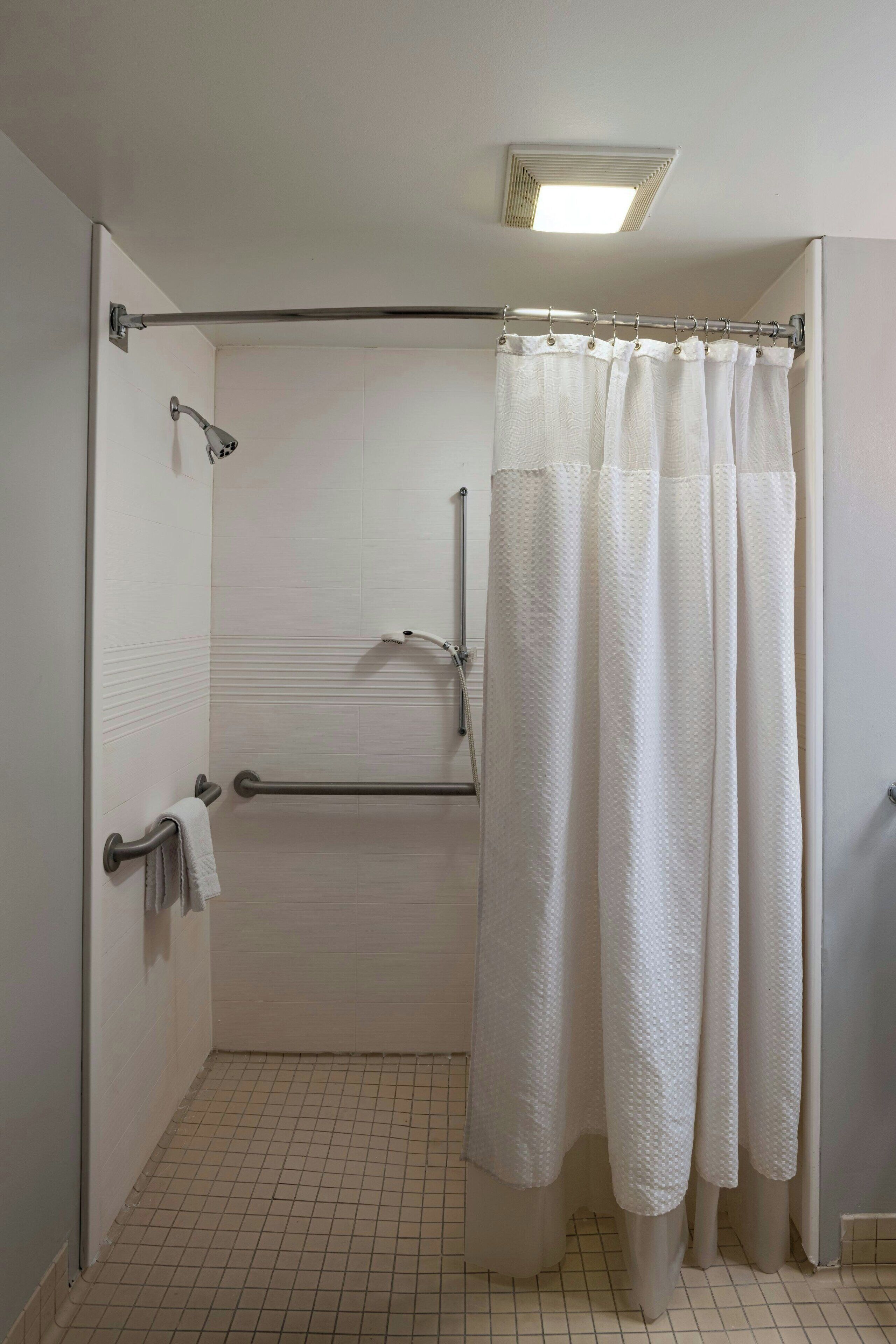 A walk-in shower with a white shower curtain, grab bars, and a towel rack.