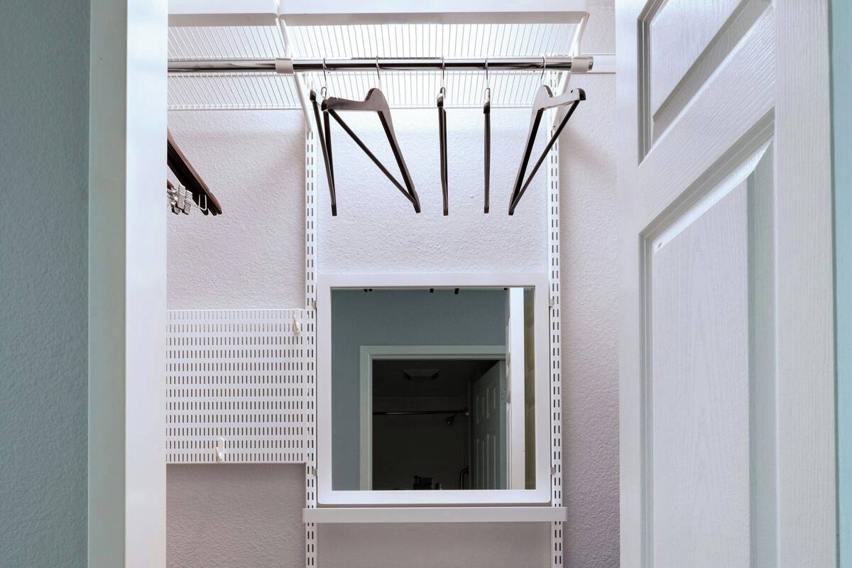 A walk-in closet with a mirrored closet rod, multiple shelves, and a vented floor.