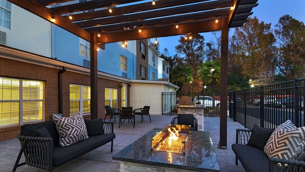 An outdoor patio with a fire feature, seating, and a pergola with string lights. - TownePlace Suites by Marriott Baton Rouge South (Baton Rouge)