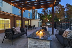 Une terrasse extérieure dotée d’un foyer, de sièges et d’une pergola illuminée de guirlandes lumineuses.