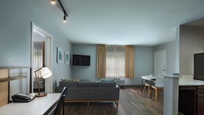 A modern hotel room with a sofa, a desk, a flat-screen TV, and a dining area. - TownePlace Suites by Marriott Baton Rouge South (Baton Rouge)