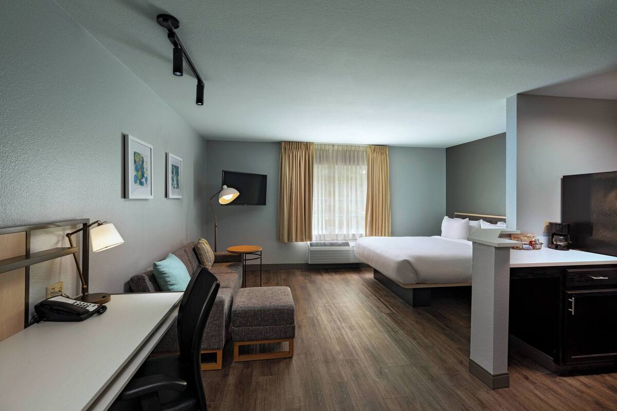 A hotel room with a desk, a bed, a sofa, and a small table.