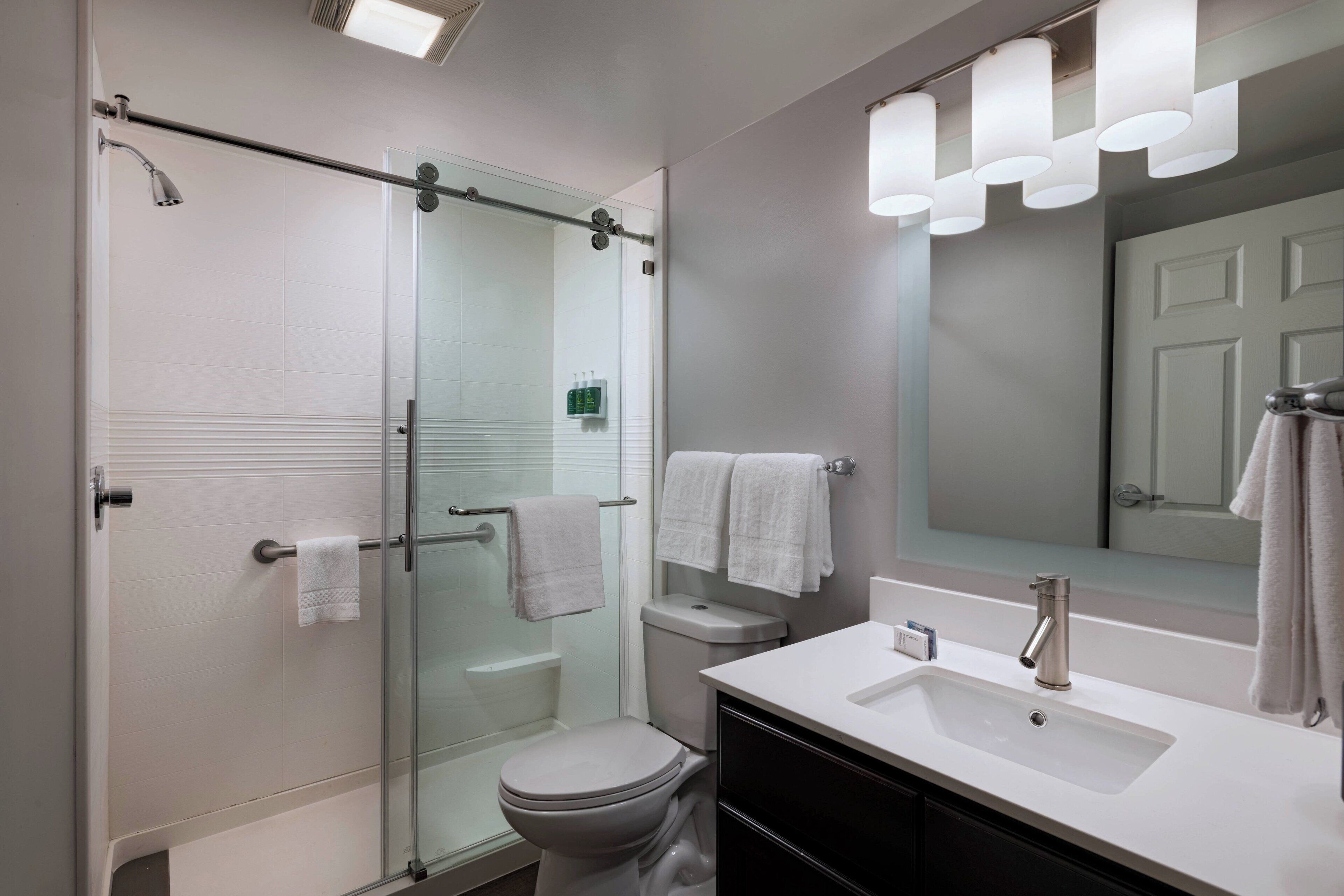A modern bathroom with a glass shower enclosure, a white toilet, a sink with a mirror, and a towel rack.