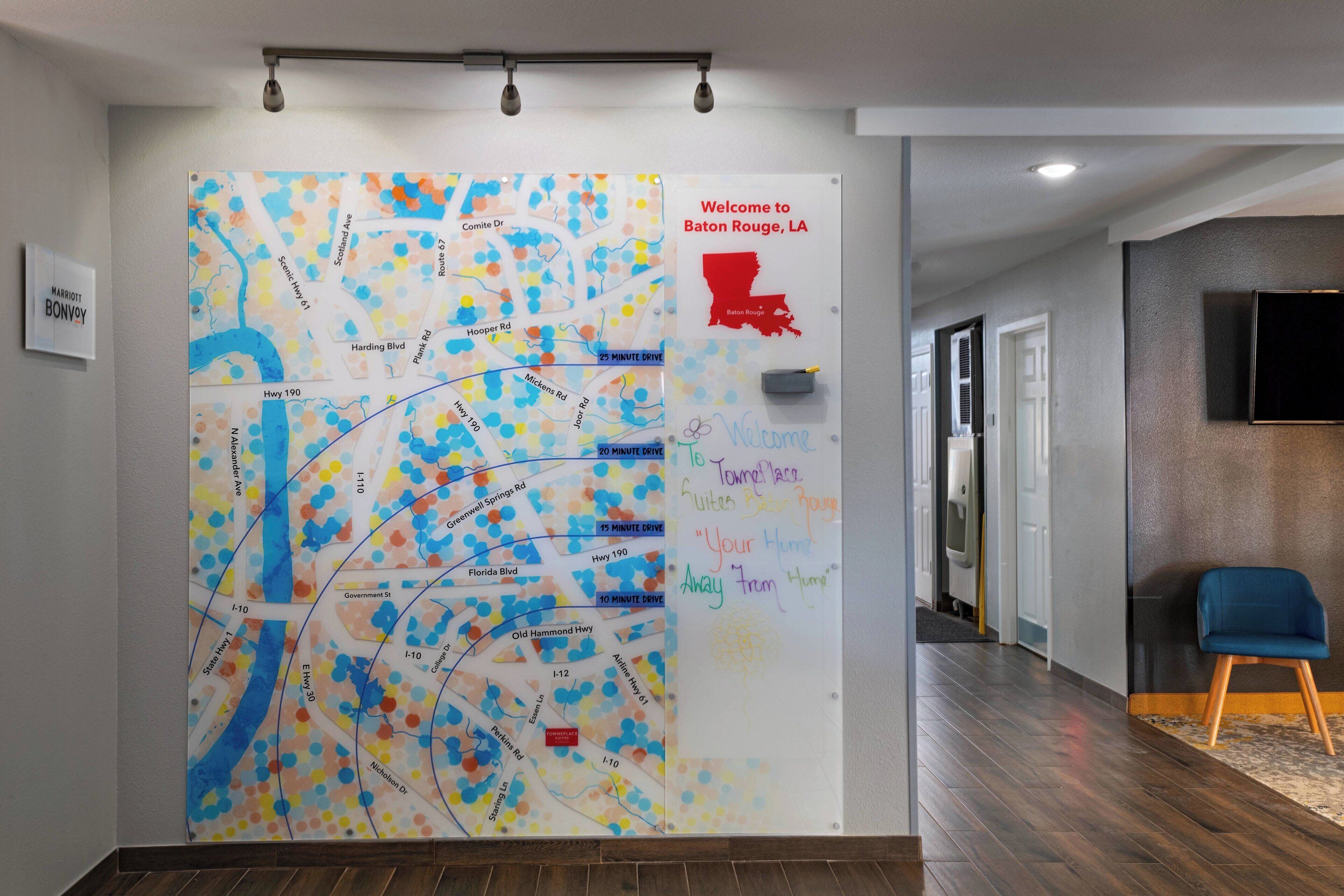 A hotel lobby with a large map on the wall, a sign welcoming guests to Baton Rouge, LA, and a blue chair.