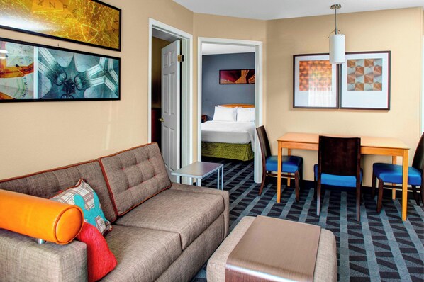 A hotel room with a sofa, a small table, a bed, and a desk with chairs.