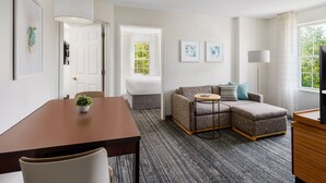 A modern hotel room with a dining table, a sofa, a small round table, and a TV. - TownePlace Suites by Marriott Manchester (Manchester)