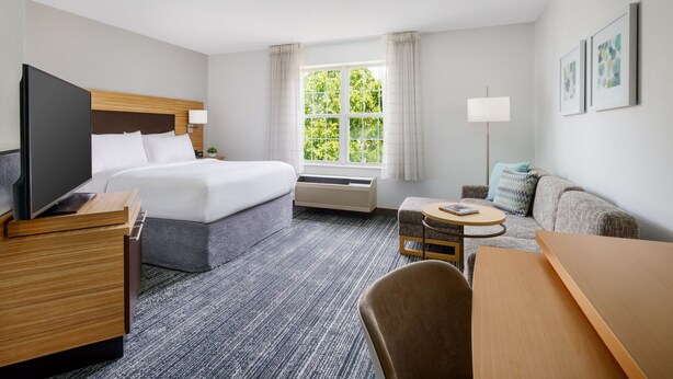 A hotel room with a bed, a desk, a chair, a TV, a lamp, and a window with curtains. - TownePlace Suites by Marriott Manchester (Manchester)