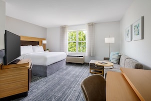 Habitación de hotel con cama, escritorio, silla, televisor, lámpara y ventana con cortinas.