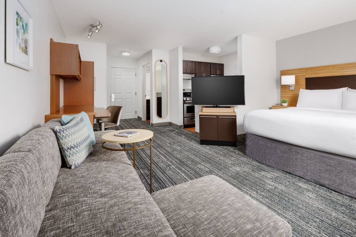 A hotel room with a sofa, a bed, a TV, a small table, and a kitchen area.