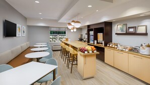 A modern dining area with round tables, a bar counter, and a kitchen area with appliances. - TownePlace Suites by Marriott Manchester (Manchester)