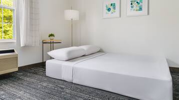 Un dormitorio ordenado con cama, mesita de noche con lámpara y dos cuadros enmarcados en la pared.