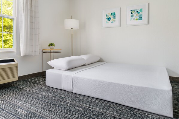 A neatly arranged bedroom with a bed, a bedside table with a lamp, and two framed artworks on the wall.