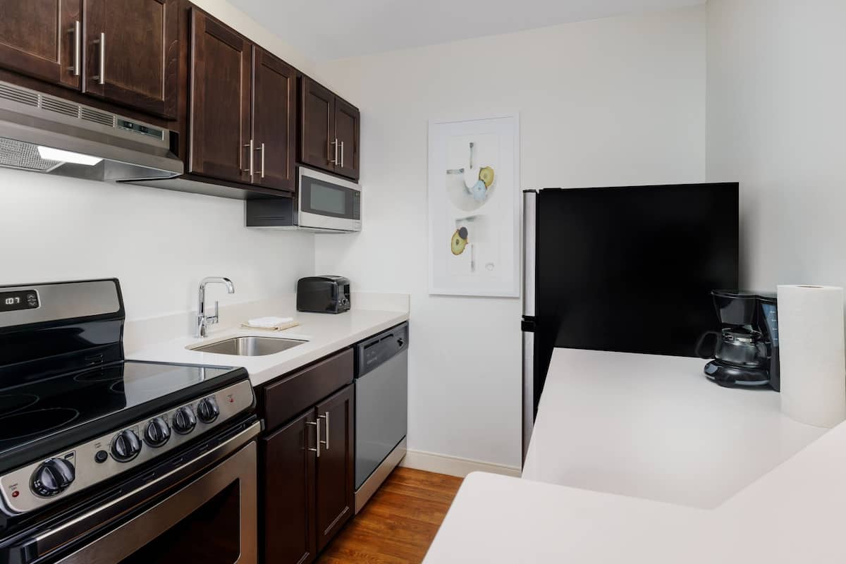 A modern kitchen with dark wooden cabinets, stainless steel appliances, and a white countertop.