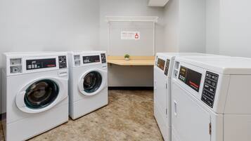 A laundry area with three front-loading washing machines and a drying rack.