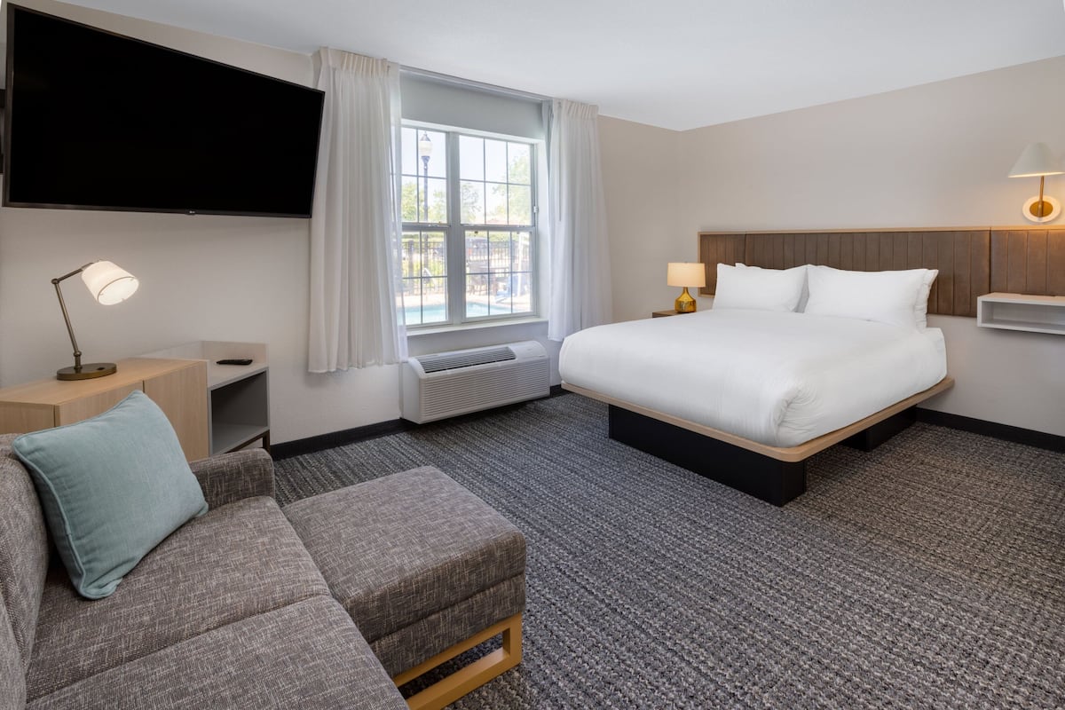 A hotel room with a large bed, a sofa, a TV mounted on the wall, and a window with curtains.