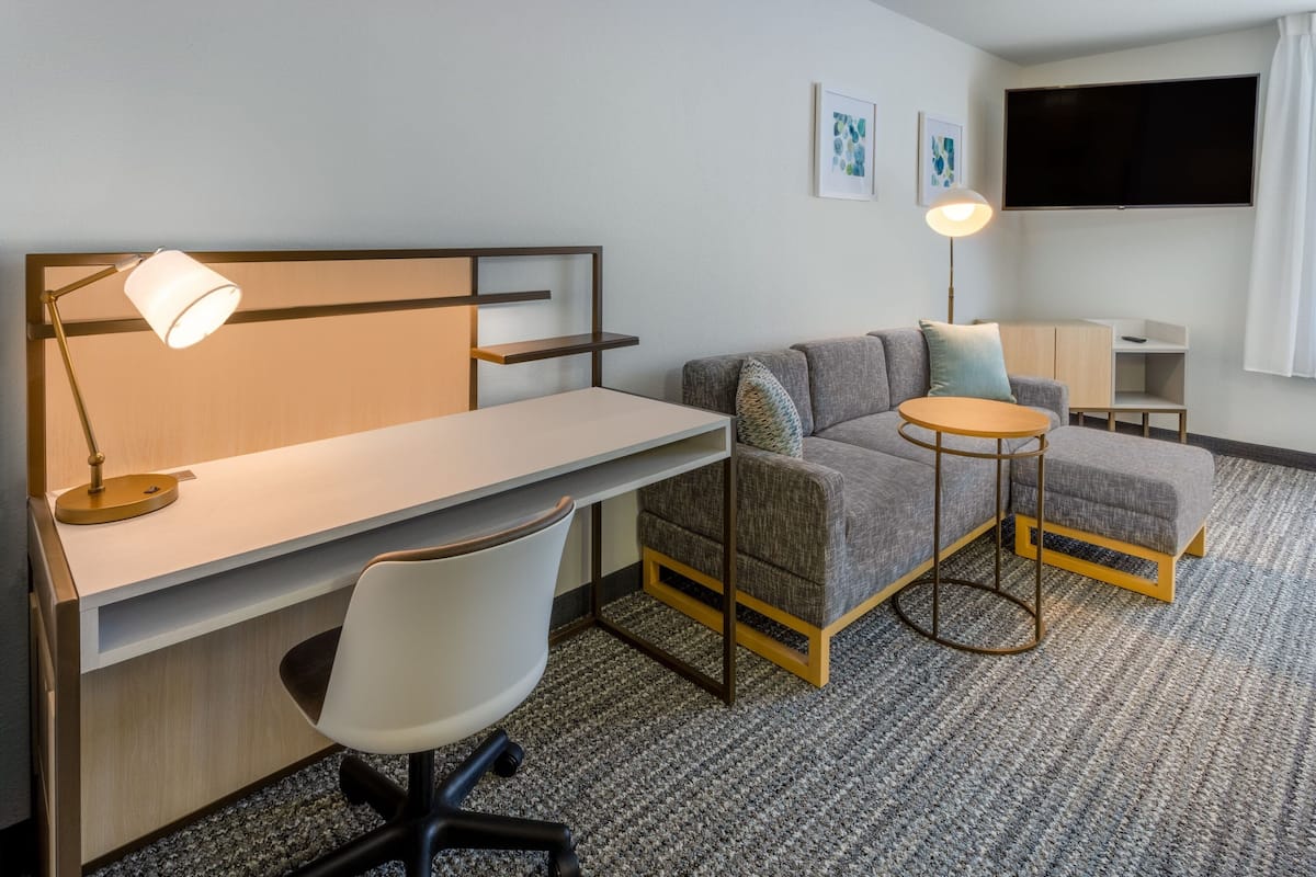 A modern hotel room with a desk, chair, sofa, and a small round table.