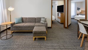 Ett modernt hotellrum med en grå soffa, ett litet bord, en lampa och en tv i hörnet.